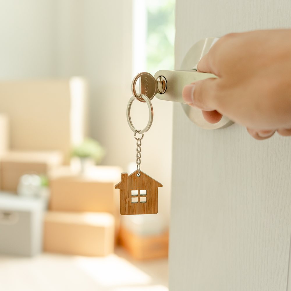 A key with a wooden house keychain unlocking the door of a new home